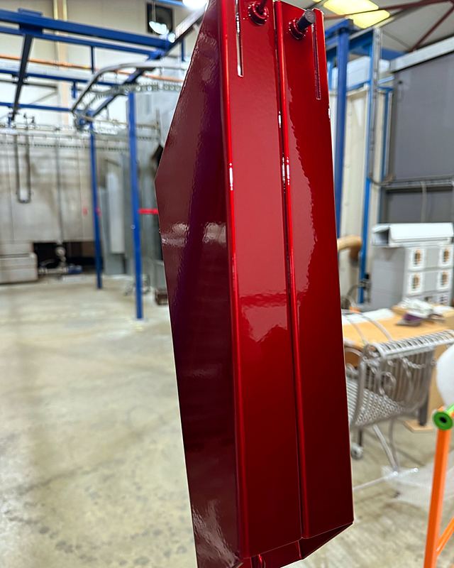 A freshly powder coated part in deep gloss red hanging on the line in the Vale workshop